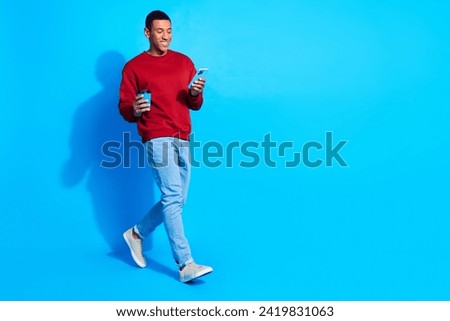 Full size profile portrait of nice person hold coffee use smart phone walk empty space isolated on blue color background