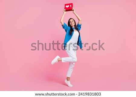 Full size photo of optimistic girl dressed blue shirt white trousers hold social media like over head isolated on pink color background