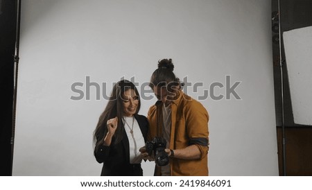Backstage of model and professional team in the studio. Male photographer and brunette woman model talking checking photos on camera together.