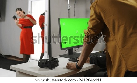 Backstage of model and professional team in the studio. Photographer and editor looking at chroma key green screen monitor, model taking selfie.