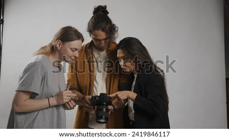 Backstage of model and professional team in the studio. Man photographer brunette woman model and female assistant checking photos on camera together.