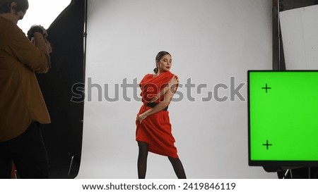 Backstage of model and professional team in the studio. Female model posing for photographer, editor table at the side chroma key green screen.