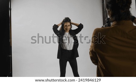 Backstage of model and professional team in the studio. Full length of appealing model in suit posing, photographer taking pics, cool expression.