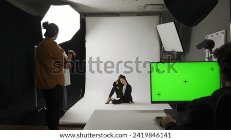 Backstage of model and professional team in the studio. Full shot female model in suit posing on the floor, editor monitor chroma key green screen.