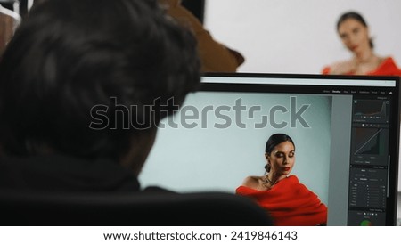 Backstage of model and professional team in the studio. Model posing on set, male editor working on computer looking at photos on monitor.