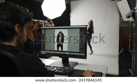 Backstage of model and professional team in the studio. Shot of male editor at monitor chroma key green screen, model and assistant stylist at the back.