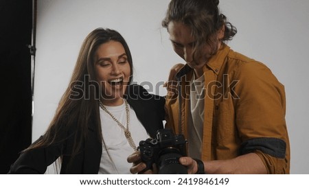 Backstage of model and professional team in the studio. Man photographer and brunette woman model looking checking photos on camera together.