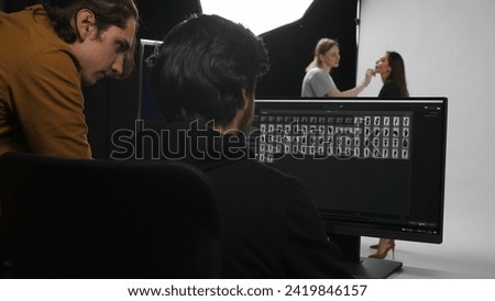 Backstage of model and professional team in the studio. Close up of model fixing makeup, photographer and editor at monitor working on photos.