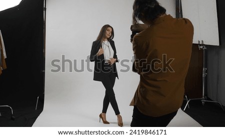 Backstage of model and professional team in the studio. Full shot attractive female model in suit posing, photographer taking pics, serious expression.