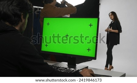 Backstage of model and professional team in the studio. Close up of editor at chroma key green screen monitor, model in suit posing for photographer.