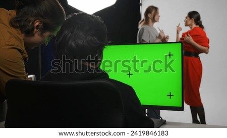 Backstage of model and professional team in the studio. Editor and photographer looking at monitor checking pictures, chroma key green screen.