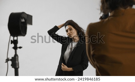 Backstage of model and professional team in the studio. Close up of attractive model in suit posing, photographer taking pics, positive expression.