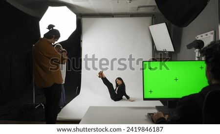 Backstage of model and professional team in the studio. Full shot appealing model in suit posing on the ground, editor monitor chroma key green screen.