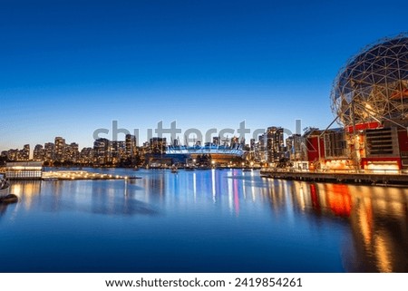 A long exposure photo during blue hour of the Vancouver Skyline from False Creek with the Science World Building and the BC Place Stadium illuminated.