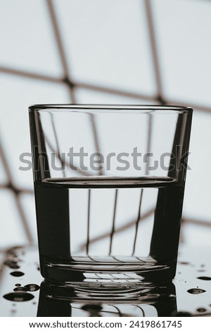 Water in a glass in selective focus in the morning or evening. Black and white window lattice background.A refreshing, chilling drink in the heat. Copy space.