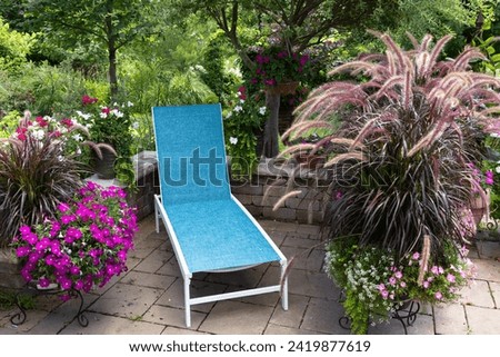A turquoise lounger and fuchsia petunias along with 
mesmerizing Purple fountain ornamental grasses in containers beckon visitors to relax on a patio on a hot summer afternoon. 
