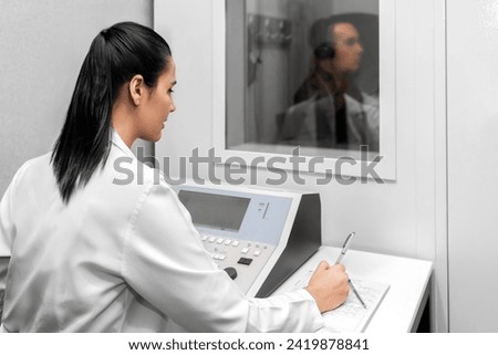Audiologist woman doing the hearing exam to a mixed race woman patient using an audiometer in a special audio room. Audiometric testing. Hearing loss treatment. Royalty-Free Stock Photo #2419878841