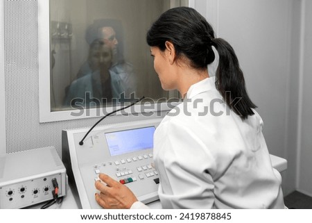 Audiologist woman doing the hearing exam to a mixed race woman patient using an audiometer in a special audio room. Audiometric testing. Hearing loss treatment. Royalty-Free Stock Photo #2419878845