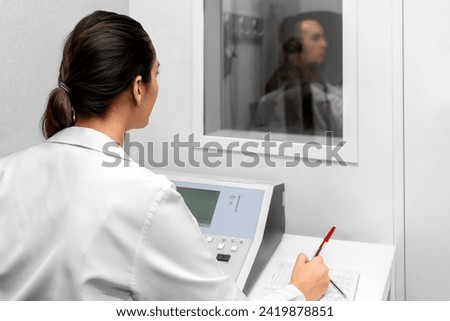 Audiologist woman doing the hearing exam to a mixed race man patient using an audiometer in a special audio room. Audiometric testing. Hearing loss treatment. Royalty-Free Stock Photo #2419878851