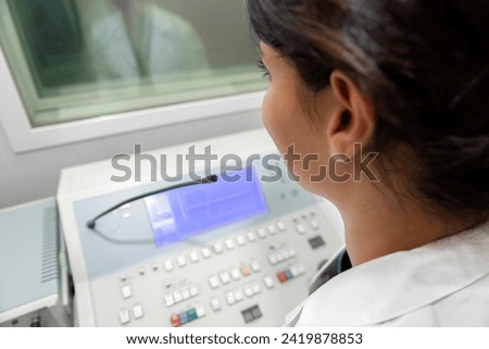 Audiologist woman doing the hearing exam to a mixed race woman patient using an audiometer in a special audio room. Audiometric testing. Hearing loss treatment. Royalty-Free Stock Photo #2419878853