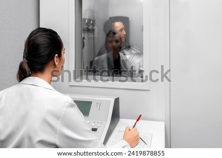 Audiologist woman doing the hearing exam to a mixed race man patient using an audiometer in a special audio room. Audiometric testing. Hearing loss treatment. Royalty-Free Stock Photo #2419878855