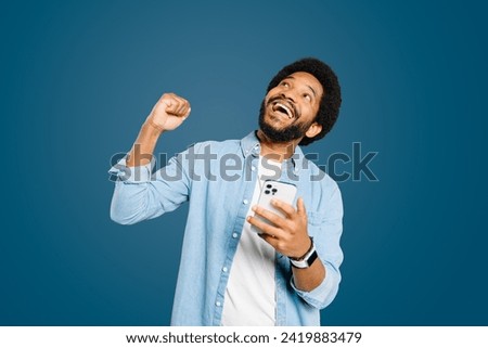 Man is captured in moment of elation, looking upwards and fist pumping air after a successful digital interaction or a win. This portrays a strong emotional response to positive digital communication. Royalty-Free Stock Photo #2419883479