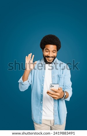Friendly and cheerful Brazilian man smiling and waving at his smartphone, illustrating the warmth and friendliness of connecting with loved ones digitally. Virtual meeting and video call concept