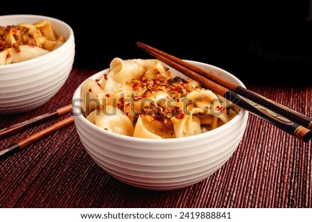 Biang Biang Noodles Topped with Spicy Chili Oil Sauce Close-up: Biang biang mian topped with minced pork and chili oil served in bowls with chopsticks Royalty-Free Stock Photo #2419888841