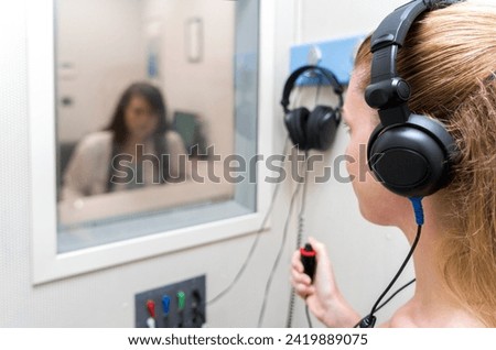 Audiologist woman doing the hearing exam to a mixed race woman patient using an audiometer in a special audio room. Audiometric testing. Hearing loss treatment. Royalty-Free Stock Photo #2419889075