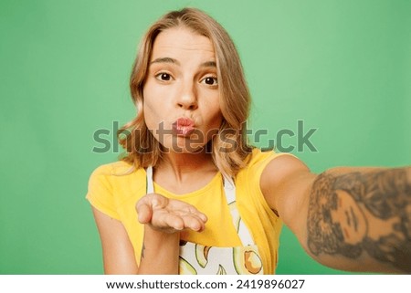 Close up young housewife housekeeper chef cook baker woman wear apron yellow t-shirt do selfie shot on mobile cell phone send air kiss isolated on plain green background studio. Cooking food concept