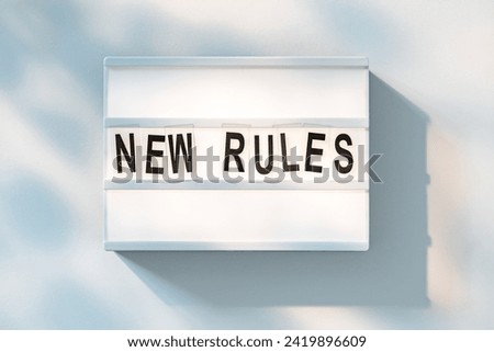 A white lightbox with bold black letters spelling out New Rules is captured with a light background suggesting a change or announcement.