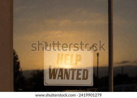 Help Wanted signage in the storefront window during sunset. America's labor shortage, labor costs, and other service occupation employment problems concepts. 