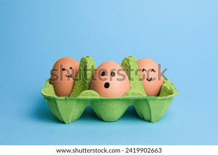 Cute easter eggs with funny faces in green box isolated on light blue background. Happy easter concept.