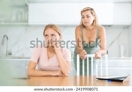 Saddened offended teen girl listening to disapproving words of mother standing in home kitchen. Concept of tension and disagreement arising between parents and child Royalty-Free Stock Photo #2419908071