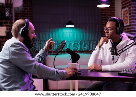 African american influencer recording podcast with guest, using audio recording equipment in home studio. Cheerful men chatting live during broadcasting session for internet show
