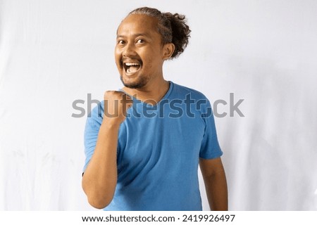 Happy excited and smiling young Asian man raising his arm up to celebrate success or achievement. isolated white