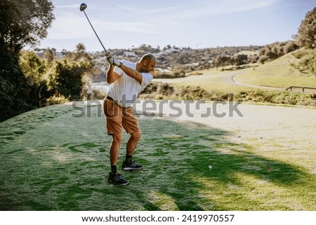 Sotogrante, Spain - January 25, 2024 - Golfer at the end of a swing on a tee box, with a golf course and hilly landscape in the background.