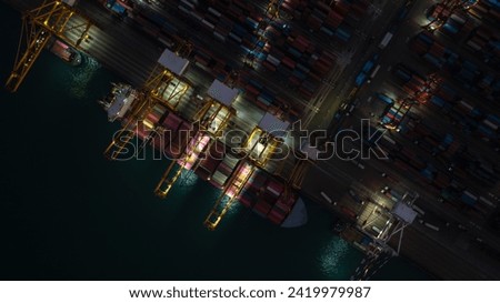 night scene shot from above commercial port loading and unloading cargo from container ship import and export by crane for distributing goods by trailers transported to customers and dealers top view