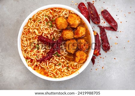 spicy instant noodles or ramen with fish balls and dried chili on mottled grey backdrop with copy space. Flat lay, top view.
