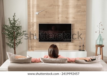 Girl in on the sofa in the living room in front of the TV. Royalty-Free Stock Photo #2419992457