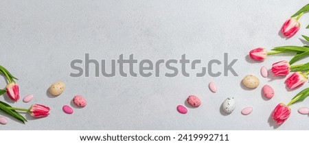 Pink tulips with Easter eggs on light stone concrete background. Festive concept, greeting card, flat lay, hard light, dark shadow, banner format