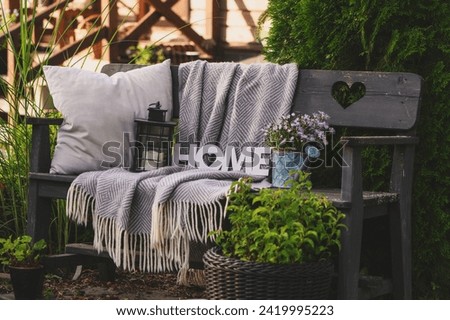 pillows and blanket on cozy rustic wooden bench in summer garden. Country living. Royalty-Free Stock Photo #2419995223