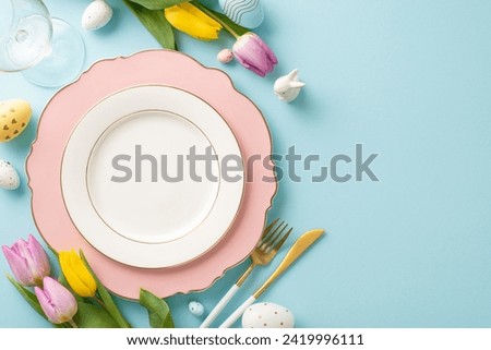 Festive Dining Scene: Overhead photo capturing an Easter-themed table setting with plate, cutlery, wine glass, tulips, ceramic bunny and colorful eggs. Pastel blue backdrop, perfect for text