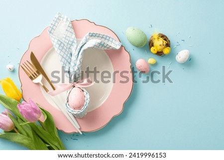 Easter enchantment: top view bunny ears napkin, cutlery, tiny chicken in nest, bunch of tulips, sprinkles, and eggs compose a delightful table setting. Pastel blue backdrop enhances the festive mood