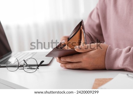 Man with empty wallet at white table indoors, closeup