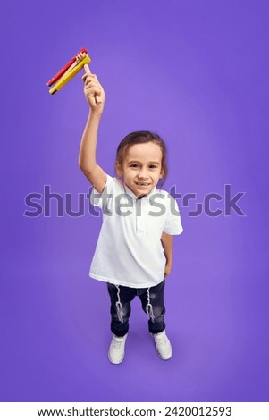 Top view photo of little boy, Jewish kid looking at camera and shows grogger to camera against purple background. Purim, business, festival, holiday, celebration, judaism, religion concept. Ad