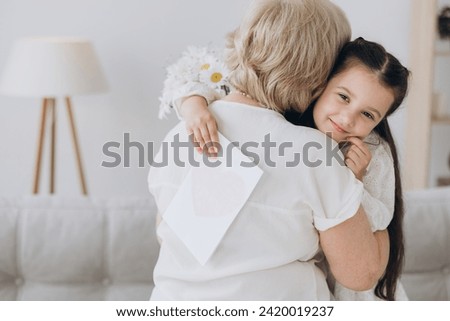 I Love You, Granny. Portrait of cute little girl embracing her grandmother in cheek giving bunch of flowers and postcard, greeting woman with holiday, Women's or Mother's Day or birthday.