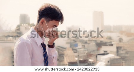 A  young man wearing face masks to protect PM 2.5 smoke, city dust danger and air pollution in city,  factory pipes and industrial smog.  toxic mist. Protection against smoke. covid-19 protection. Royalty-Free Stock Photo #2420022913