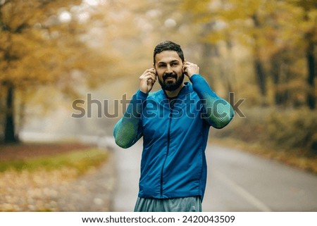 Portrait of a happy runner putting earphones and preparing for exercise in nature.