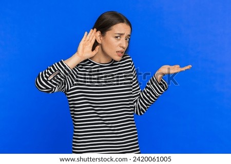 I cant hear you. What. Young Caucasian woman trying hear you looking confused and frowning keeping arm near ear for louder voice asking to repeat to hear information deafness. Girl on blue background Royalty-Free Stock Photo #2420061005